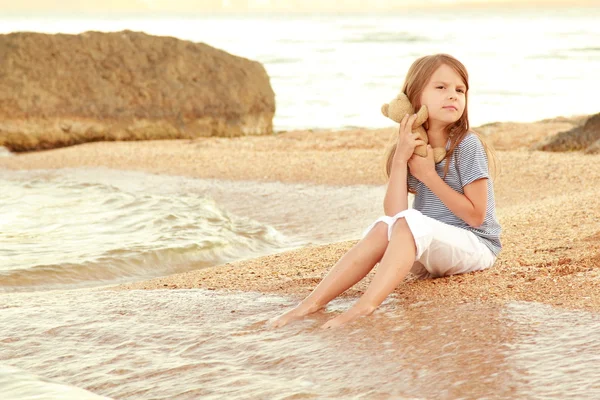 Menina bonita com cabelos longos e pele saudável na costa do mar e molha os pés na água . — Fotografia de Stock