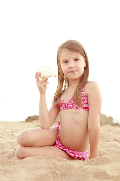 Menina feliz bonito com um sorriso encantador brincando na areia com uma concha — Fotografia de Stock