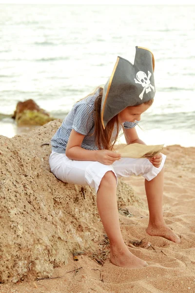 Hermosa niña alegre en un traje de pirata está estudiando un mapa del tesoro —  Fotos de Stock