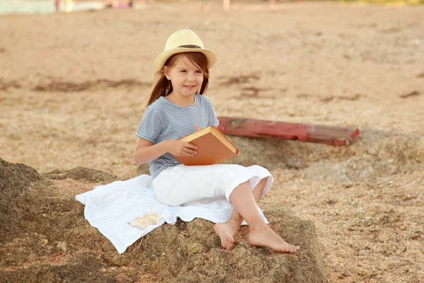 Adorable little girl reading book near the ocean