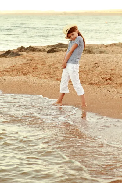 Positiv lächelndes kleines Mädchen am Strand nass Füße im Wasser bei Sonnenuntergang im Freien — Stockfoto