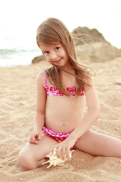 Caucasian happy young girl in a pink swimsuit sitting on the beach — Stock Photo, Image