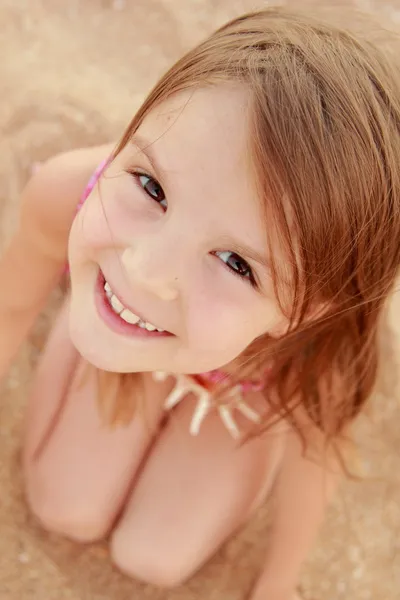 海砂の背景にかわいい小さな女の子が水着の笑みを浮かべて座っています。 — ストック写真