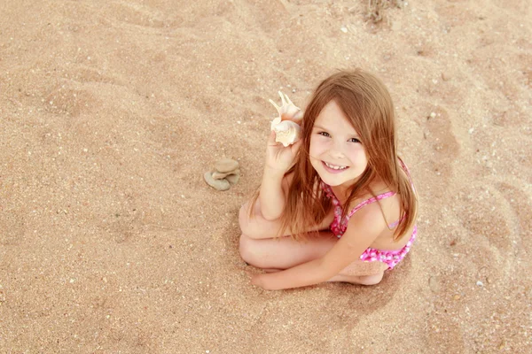 Ładny, uśmiechnięta dziewczynka w kostiumie kąpielowym siedzi na tle morza piasek — Zdjęcie stockowe