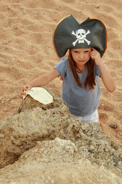 Menina bonito em um chapéu de pirata com um mapa pirata na mão — Fotografia de Stock