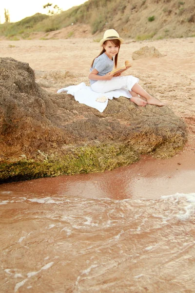 Kaukasisch lächelndes junges Mädchen in lässiger Kleidung liest am Strand ein Buch — Stockfoto