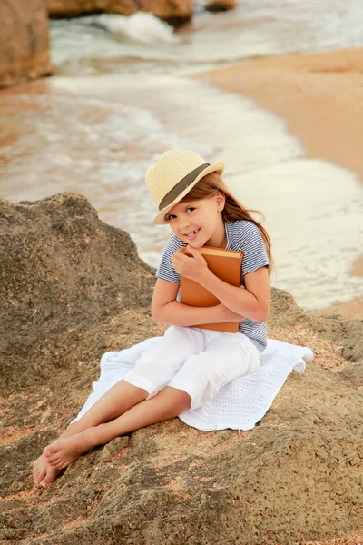 Mooi positieve meisje met een charmante glimlach lezen van een boek op het strand — Stockfoto