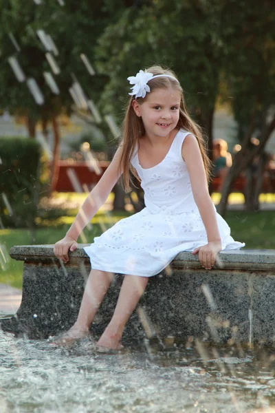 Hermosa niña en un vestido blanco cerca de la fuente en el caluroso día de verano al aire libre —  Fotos de Stock