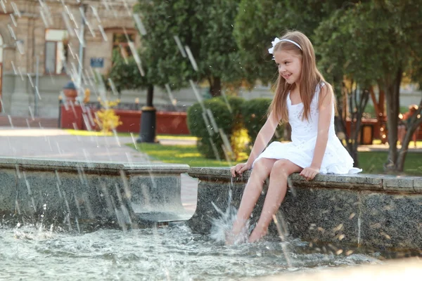 Glada unga tjej med vackra hår kissar fötter i en fontän på en varm sommardag — Stockfoto