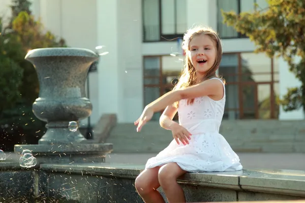 Joyful young girl with beautiful hair wets feet in a fountain on a hot summer day — Stock fotografie