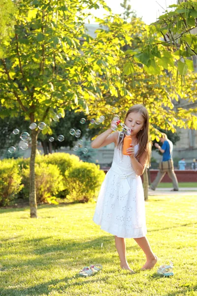 Menina bonito está soprando uma bolhas de sabão. — Fotografia de Stock