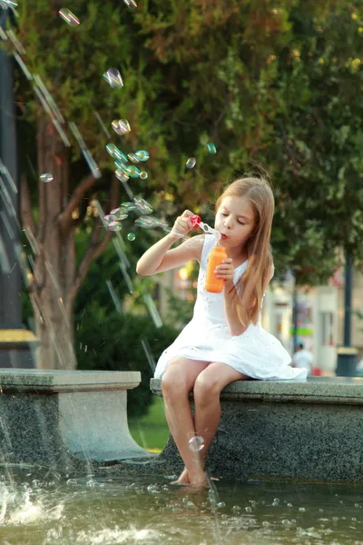 Europäisches Mädchen im weißen Kleid bläst Seifenblasen im Sommerpark. — Stockfoto