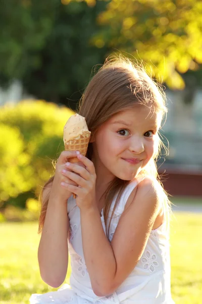 草の上に座って、アイスクリームを食べる白いドレスで甘い笑顔で魅力的な少女 — ストック写真