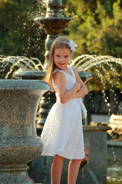 Thoughtful little casual girl standing near city fountain — Stock Photo, Image