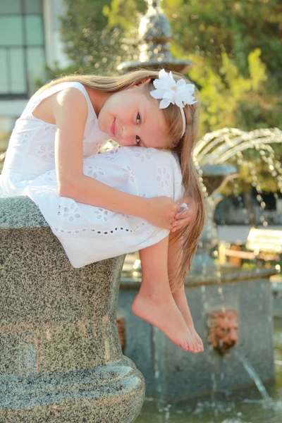 Joyful smiling little girl with beautiful hairstyle dreams near the fountain — Stock Photo, Image