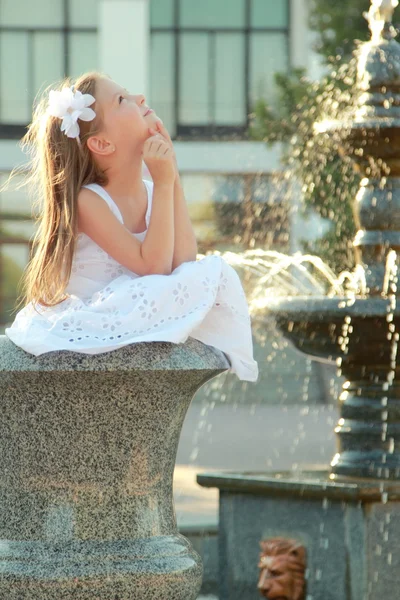 Joyeuse petite fille souriante avec de beaux rêves de coiffure près de la fontaine — Photo