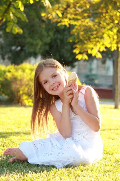 Jovem encantadora com um sorriso doce em vestido branco sentado na grama e comer sorvete — Fotografia de Stock