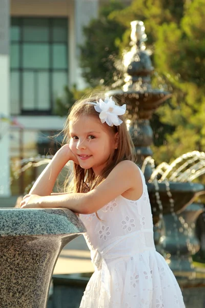 Hermosa niña en un vestido blanco cerca de la fuente en el caluroso día de verano al aire libre —  Fotos de Stock