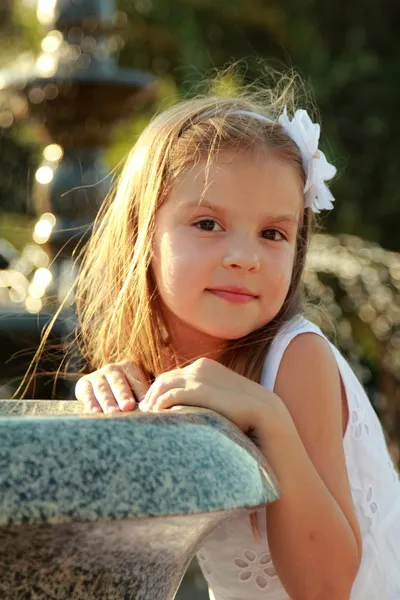 Glada leende liten flicka med vacker frisyr drömmar nära fontänen — Stockfoto