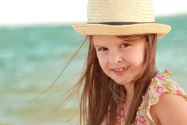 Portrait of a little girl who dreams of a hat on a background of a sea landscape outdoors. Stock Picture