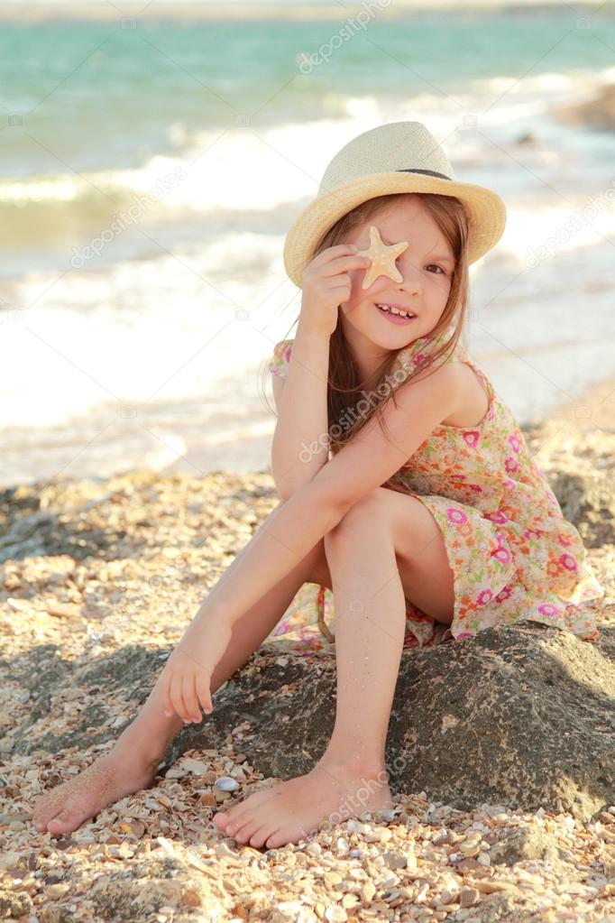 Smiling young girl holding a starfish sitting on the bank of the summer sea.