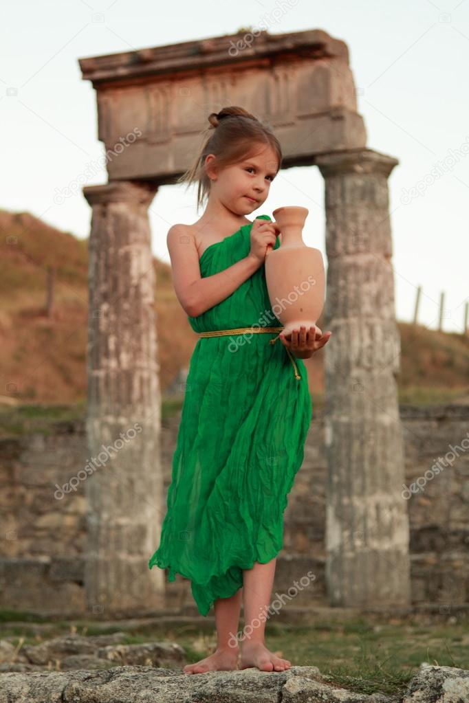 Beautiful young Greek goddess in emerald green vintage dress holding of an ancient amphora.