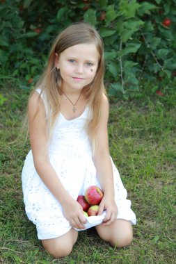 çimenlerin üzerinde oturan ve elma tutan küçük kız