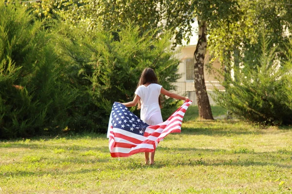 Χαρούμενη το όμορφο κορίτσι σε ένα λευκό φόρεμα, κρατώντας μια μεγάλη αμερικανική σημαία — Φωτογραφία Αρχείου