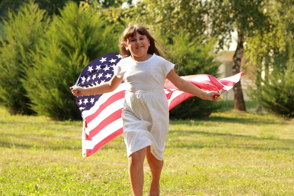 Joyful pretty young girl holding a big a U.S. flag — Stock Photo, Image