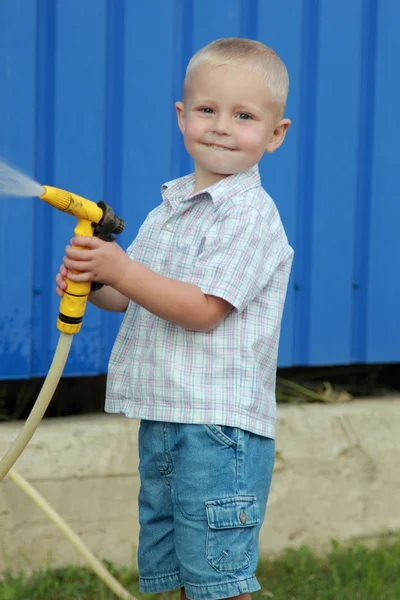 Kleine blonde jongen drenken het gazon — Stockfoto