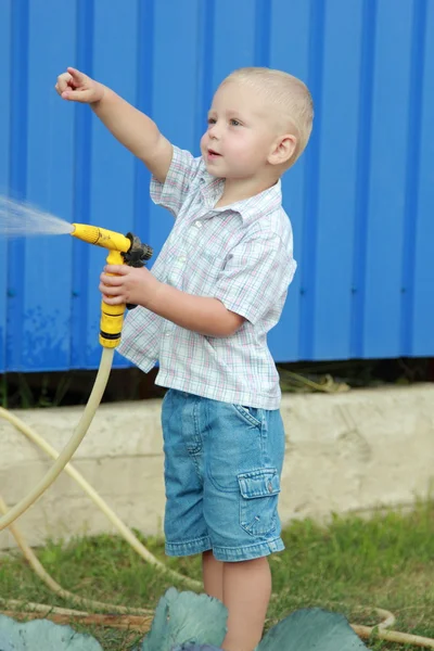 Kleiner blonder Junge wässert den Rasen — Stockfoto