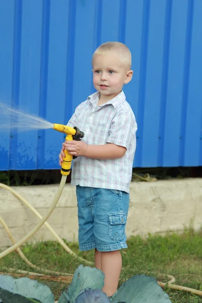 Kleiner blonder Junge wässert den Rasen — Stockfoto