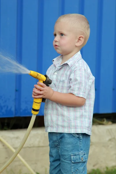 Kleiner blonder Junge wässert den Rasen — Stockfoto