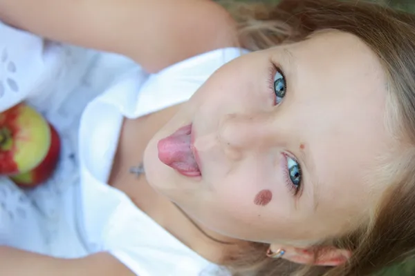 Niña sentada en la hierba y sosteniendo manzanas — Foto de Stock