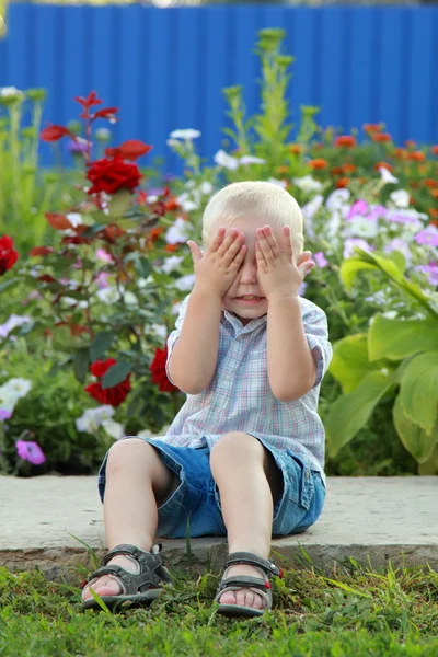 Blonde jongen speelt op de achtergrond van bloemen — Stockfoto