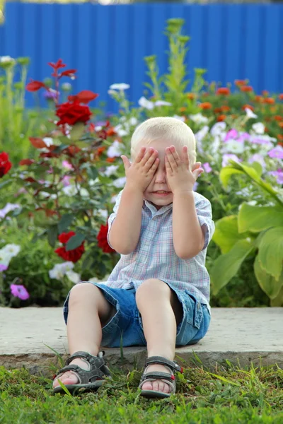 Rubio chico está jugando en el fondo de las flores — Foto de Stock