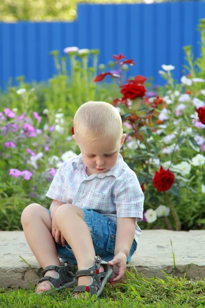 Blond boy spelar på bakgrund av blommor — Stockfoto