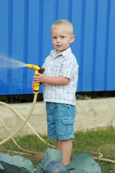 Little blond boy watering the lawn — Stock Photo, Image