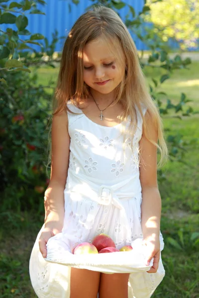 Kleines Mädchen sitzt auf Gras und hält Äpfel — Stockfoto