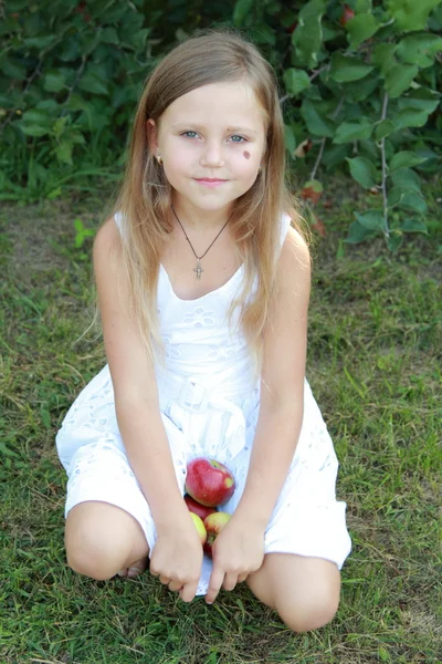 Liten flicka sitter på gräset och hålla äpplen — Stockfoto