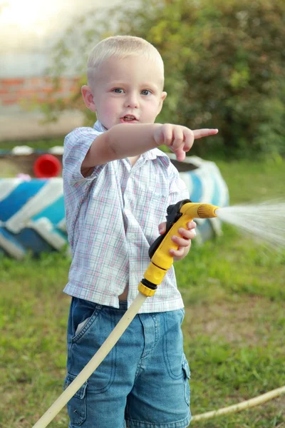 Glücklicher kleiner Junge gießt Wasser aus einem Schlauch — Stockfoto