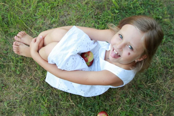 Piękna, uśmiechnięta dziewczynka w białej sukni siedzi na trawie — Zdjęcie stockowe