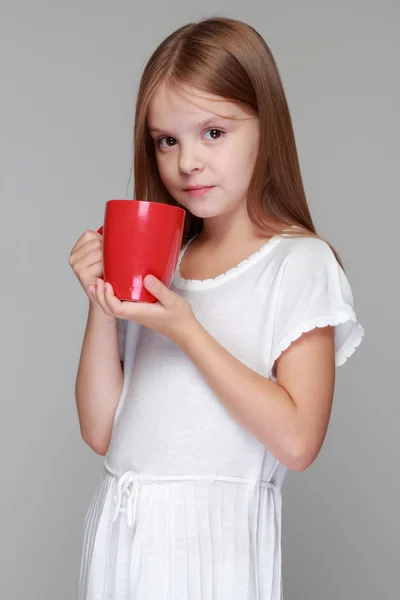 Kleines Mädchen trinkt Tee aus einer roten Tasse — Stockfoto