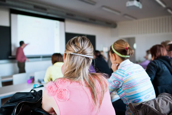 Ung, ganska kvinnlig collegestudent som sitter i ett klassrum fullt — Stockfoto