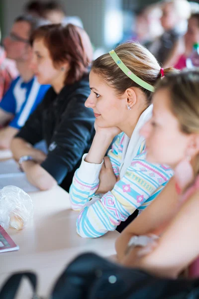 Fiatal, csinos női főiskolai hallgató ül egy osztályteremben teljes — Stock Fotó