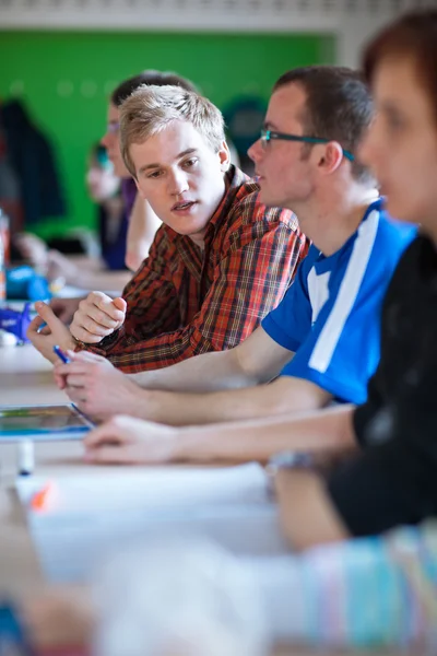 Junge, gut aussehende College-Studentin sitzt in einem Klassenzimmer voller s — Stockfoto