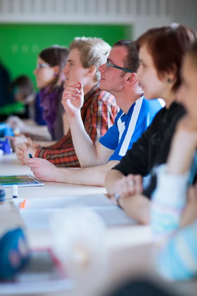 Junge, gut aussehende College-Studentin sitzt in einem Klassenzimmer voller s — Stockfoto