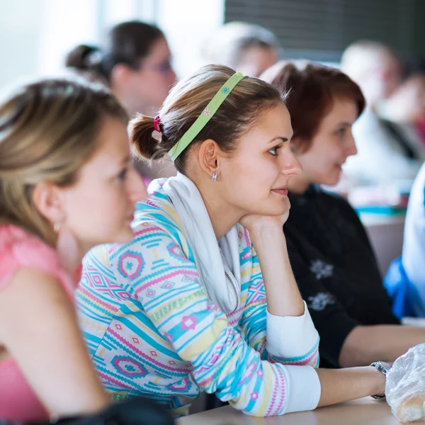 Ung, ganska kvinnlig collegestudent som sitter i ett klassrum fullt — Stockfoto