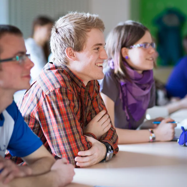 Junge, gut aussehende College-Studentin sitzt in einem Klassenzimmer voller s — Stockfoto