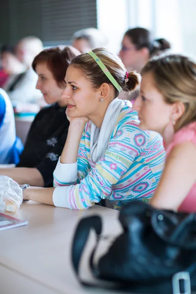 Giovane, bella studentessa universitaria seduta in una classe piena — Foto Stock